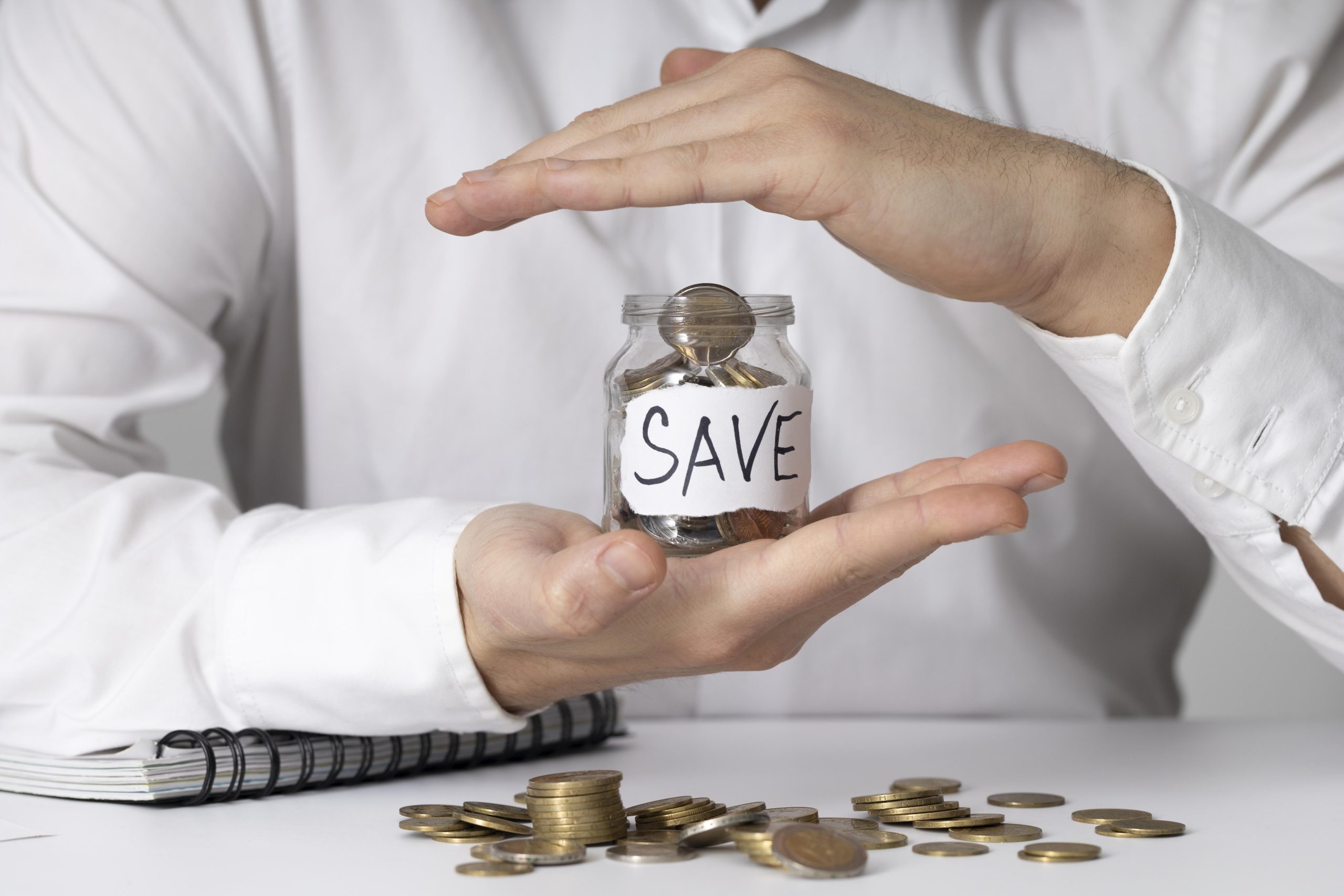 A person in a white shirt carefully holds a glass jar labeled "SAVE" filled with coins, symbolizing the importance of saving money and controlling costs through intentional budgeting and financial discipline.
