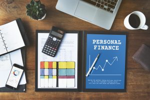 A workspace featuring a blue folder labeled "Personal Finance," a calculator, documents, a smartphone with graphs, a planner, and a laptop, symbolizing the tools and strategies needed to organize finances effectively.