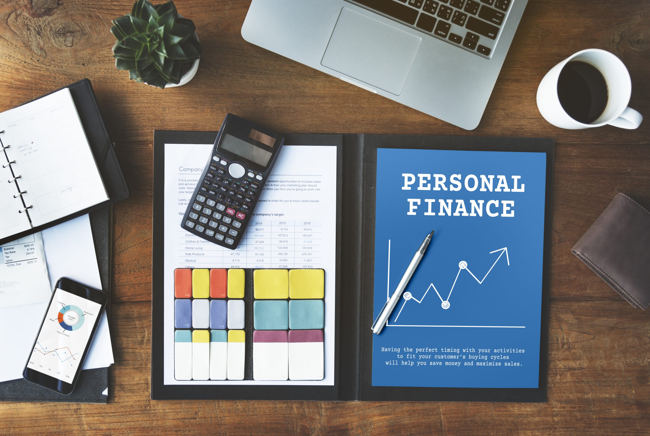 A workspace featuring a blue folder labeled "Personal Finance," a calculator, documents, a smartphone with graphs, a planner, and a laptop, symbolizing the tools and strategies needed to organize finances effectively.