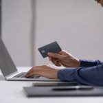 Man using a laptop at a minimalist desk while holding a dark bank card in a modern, well-lit environment, representing digital credit analysis and online financial services in the United States.
